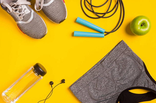 Fitness accessories on yellow background. Sneakers, bottle of water, headphones and sport top. - 写真・画像