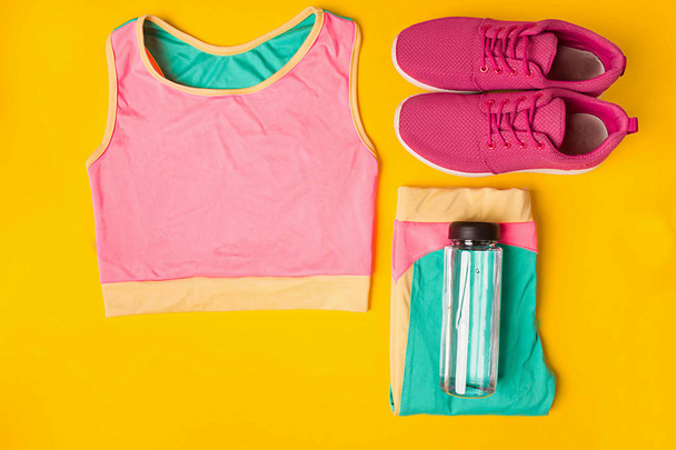 Sport equipment. Sneakers and bottle of water on yellow background - Photo, Image