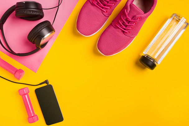 Fitness accessoires op gele achtergrond. Sneakers, fles water, hoofdtelefoons en smart. - Foto, afbeelding