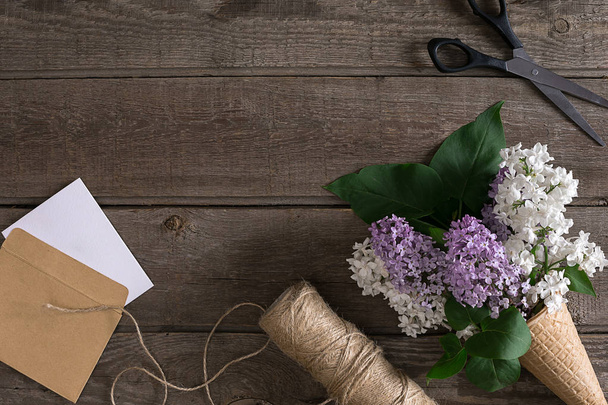 Flor de lila sobre fondo rústico de madera con espacio vacío para el mensaje de saludo. Tijeras, carrete de hilo, sobre pequeño. Vista superior
 - Foto, Imagen