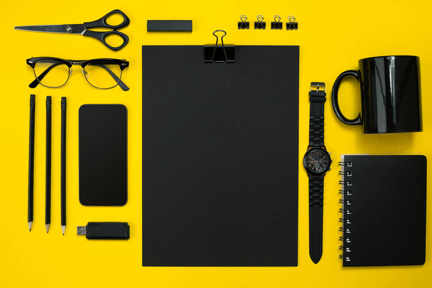 Μαύρα αντικείμενα από το γραφείο σε κίτρινο φόντο. Εργασία και τη δημιουργικότητα. Το Top view. - Φωτογραφία, εικόνα