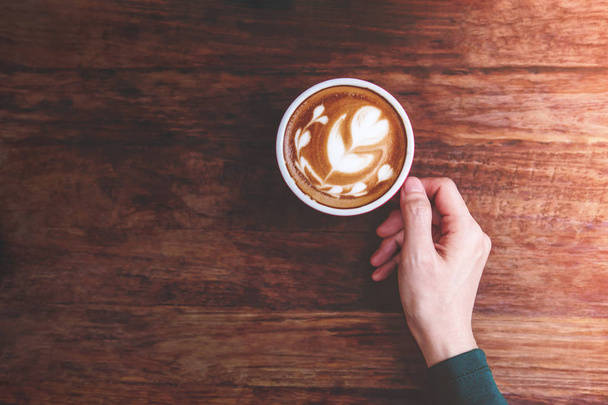 Relaxační Cozy v Cafe konceptu, ženské ruky držící horký šálek kávy Latte na dřevěný stůl, životního stylu městských lidí, pohled shora - Fotografie, Obrázek