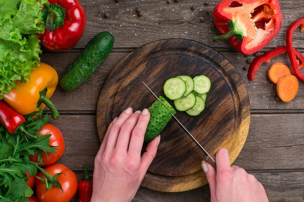 Female hands cutting cucumber at table, top view - Foto, immagini