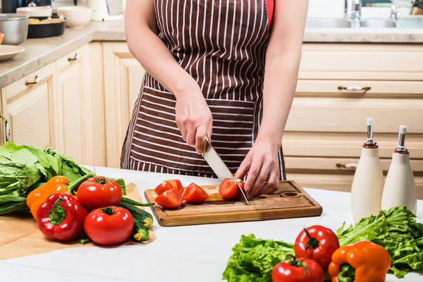 Fiatal nő főzés otthon a konyhában. Egy nő csökkenti a paradicsom és a zöldség egy késsel. - Fotó, kép