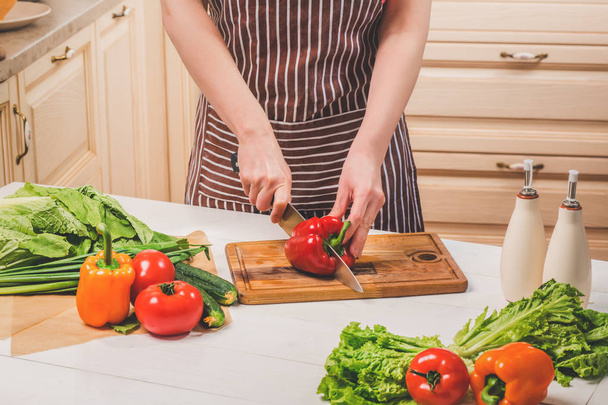 Nuori nainen kokkaamassa keittiössä kotona. Nainen leikkaa pippuria ja vihanneksia veitsellä
. - Valokuva, kuva