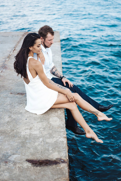 Casal jovem está sentado no cais junto ao mar - Foto, Imagem