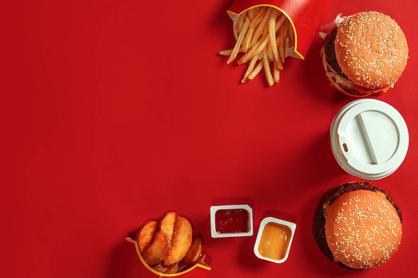 Fastfood schotel bovenaanzicht. Hamburger vlees, aardappels, chips en glas van drank op rode achtergrond. Afhaalmaaltijden samenstelling. - Foto, afbeelding
