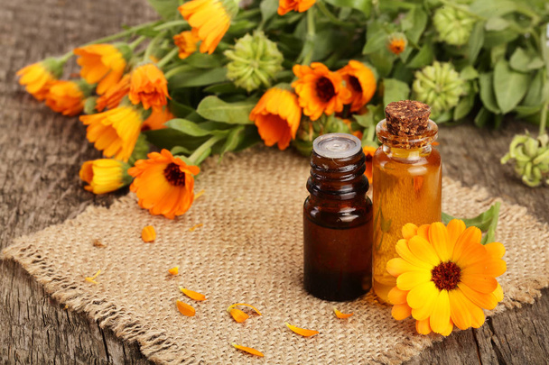 aromatherapy essential oil with fresh marigold flowers on old wooden background. Calendula oil - Fotoğraf, Görsel