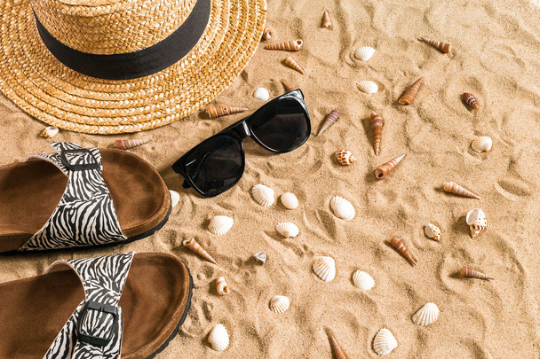 Zomer beachwear, slippers, hoed, zonnebril en schelpen op zand strand. - Foto, afbeelding