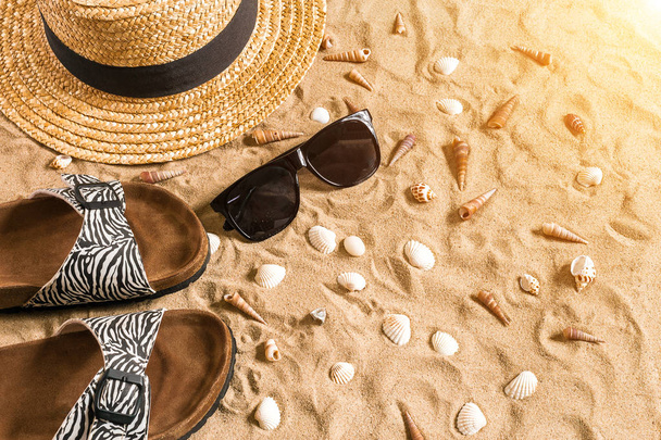 夏のビーチウェア、サンダル、帽子、サングラス、砂浜で貝殻. - 写真・画像
