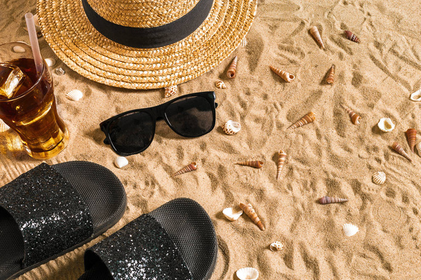 夏のビーチウェア、サンダル、帽子、ガラスと砂のビーチで貝殻に冷たい飲み物. - 写真・画像