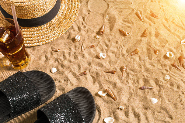 Lato, stroje kąpielowe, klapki, kapelusz, zimny napój w szklance i muszle na plaży. - Zdjęcie, obraz