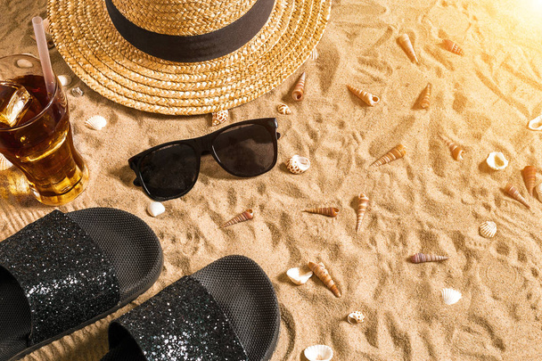 Summer beachwear, flip flops, hat, cold drink in a glass and seashells on sand beach. - Photo, Image