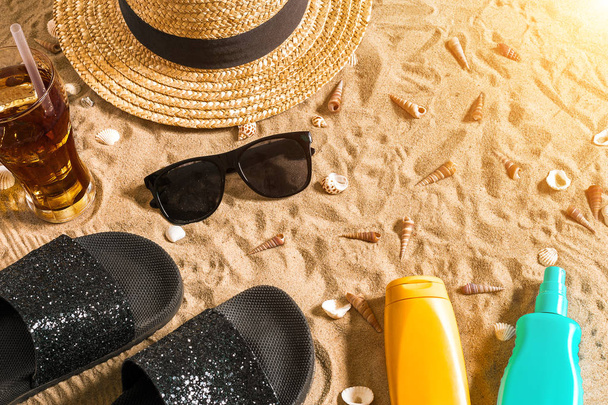 Zomer beachwear, slippers, hoed, koud drankje in een glas en schelpen op zand strand. - Foto, afbeelding