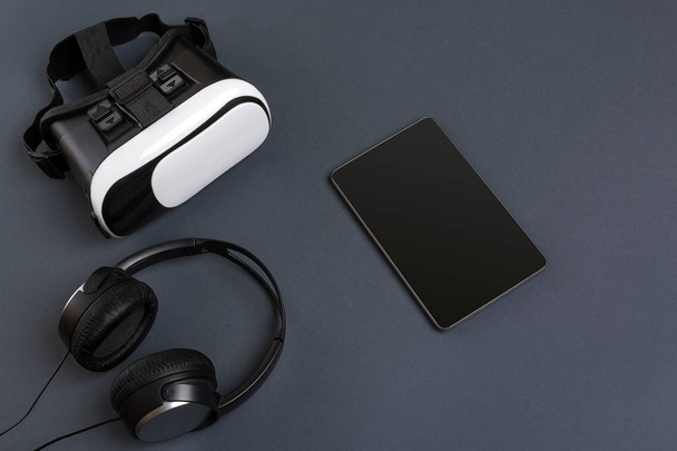 Gafas de realidad virtual y tablet con auriculares sobre fondo gris. Vista superior
 - Foto, imagen