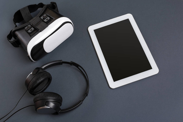 Lunettes de réalité virtuelle et tablette avec écouteurs sur fond gris. Vue du dessus
 - Photo, image