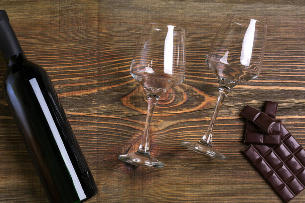Bar of chocolate, bottle and two glasses of wine on wooden background from top view - Photo, Image