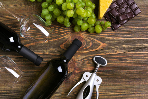 Botellas de vino tinto y blanco, uva, queso y vasos sobre mesa de madera. Vista superior con espacio de copia
 - Foto, imagen