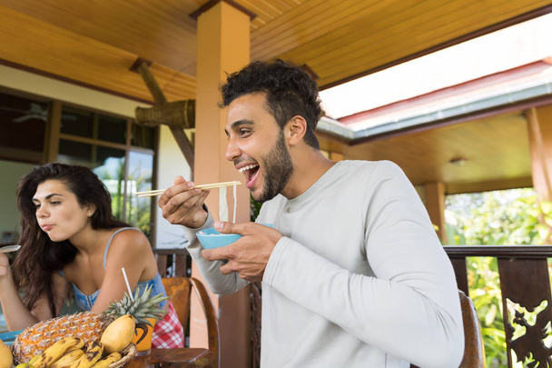 Gente alegre degustando fideos asiáticos comiendo con palillos juntos Amigos reuniéndose y comunicándose
 - Foto, Imagen
