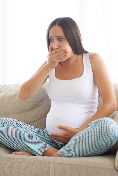 Schwangere junge Frau sitzt auf Sofa und fühlt sich krank - Foto, Bild