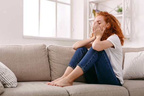Sad redhead woman thinking on beige couch - Фото, зображення