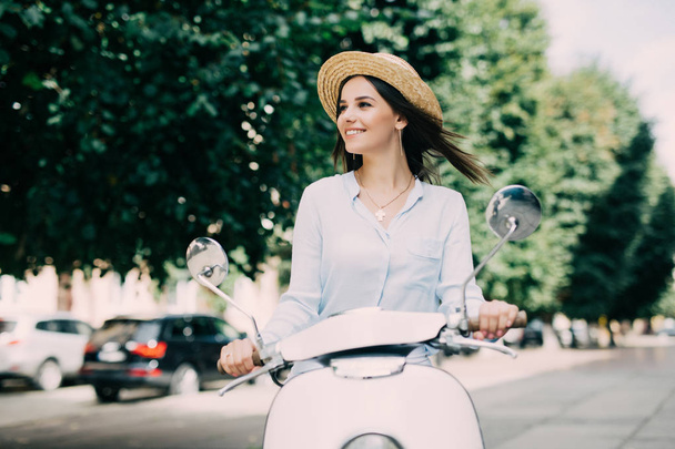 Emocionada joven y hermosa mujer montando scooter a lo largo de la calle y manteniendo la boca abierta
 - Foto, imagen