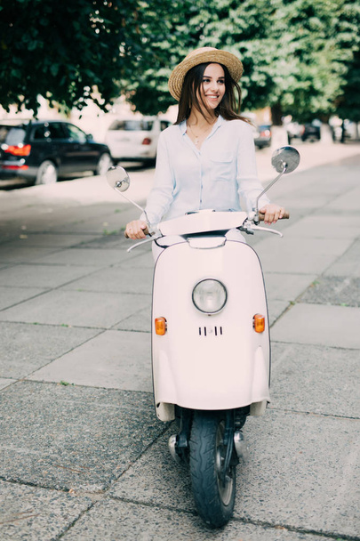 Excited young and beautiful woman riding scooter along the street - Photo, Image