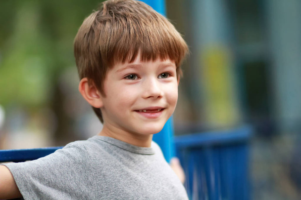 Retrato sincero de um menino feliz em camiseta cinza sorrindo e sentado no banco ao ar livre no parque. Fechar a expressão facial, turva
  - Foto, Imagem