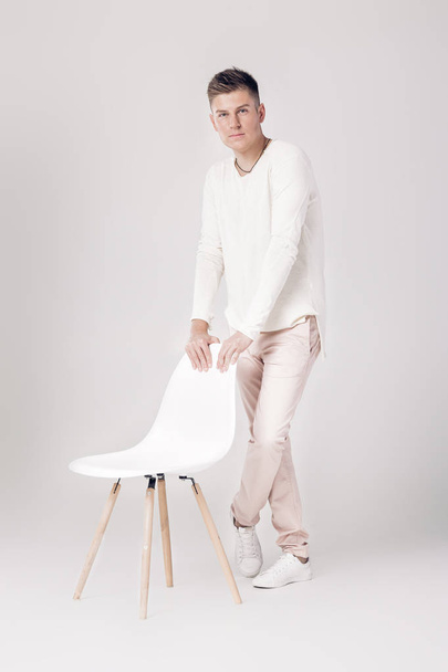 handsome young man in white sweater sits on a chair on - 写真・画像