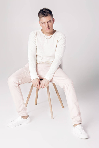 przystojny, młody człowiek w białym swetrze siedzi na krześle - Zdjęcie, obraz
