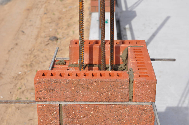Construção de tijolos. Instalando blocos de Clinker vermelho e calafetagem junções de alvenaria de tijolo coluna de tijolo exterior com haste de ferro
. - Foto, Imagem