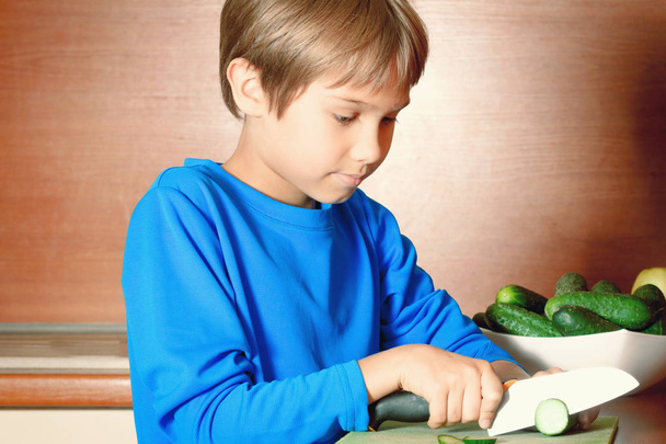 Pieni poika leikkaa vihanneksia keittiössä
 - Valokuva, kuva