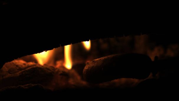 Faire et cuire des saucisses de hot-dog sur un feu de camp ouvert. Griller de la nourriture sur des flammes de feu de joie sur une branche de bois - lances de bâton dans la nature la nuit
. - Photo, image