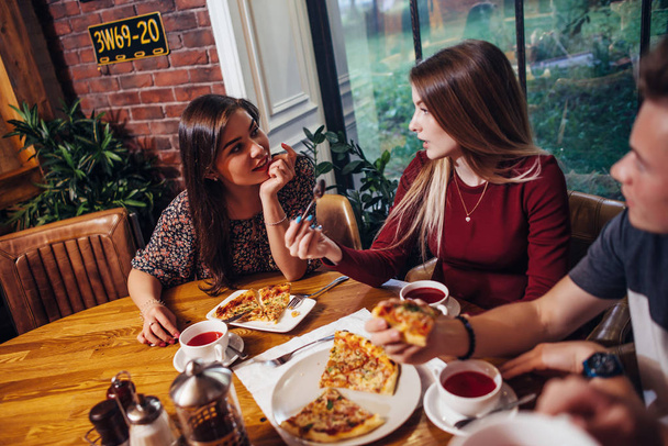 Подружки ведут разговор, едят пиццу в кафе.
 - Фото, изображение