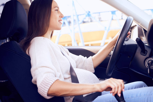 Hymyilevä raskaana oleva nainen ajaa autoa
 - Valokuva, kuva