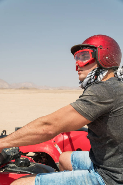 Молодой парень во время экскурсии по пустыне на квадроциклах - Человек в шлеме и приключенческая одежда в экзотических сценариях - Концепция активного отдыха, свободы и приключений
 - Фото, изображение