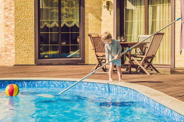 Toddler boy cleans the pool and pulls the ball out of the pool - Foto, imagen