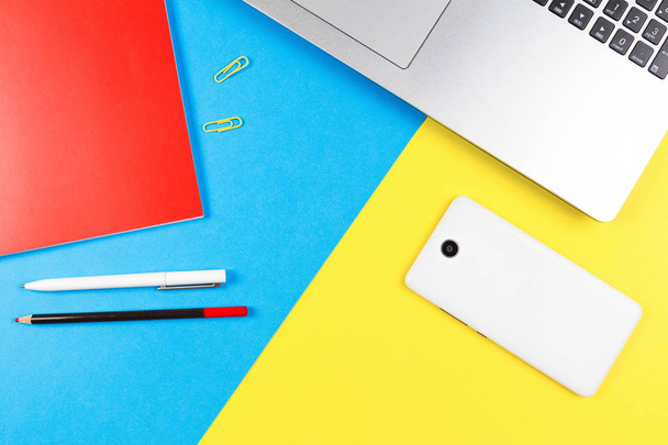 Draufsicht auf Laptop, Papier-Notizbuch, Bleistift und Stift auf blauem und gelbem Hintergrund - Foto, Bild