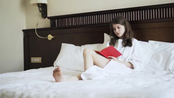 Young woman reading a book in bed, side view - Materiaali, video