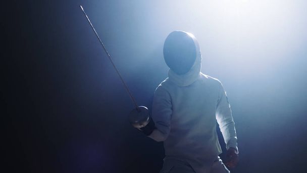 Fully Equipped Fencer Puts Lifts Foil Sword in Readiness for a Match. He Stands in the Spotlight while Darkness is Around Him. Shot Isolated on Black Background. - Foto, Bild