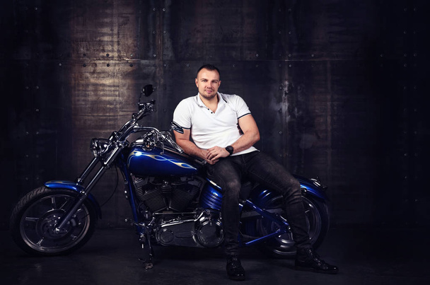 Módní portrét pohledný mladý atletický muž sedící na lesklé cool motorku v garáži - Fotografie, Obrázek