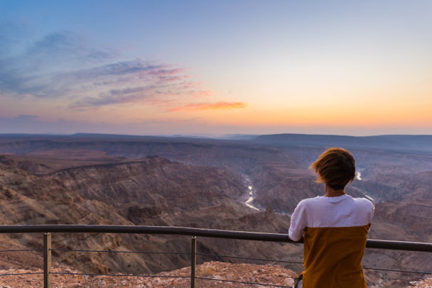 Tourist looking at the Fish River Canyon, scenic travel destination in Southern Namibia. Ultra wide angle view from above, colorful scenic sunset. - Фото, зображення