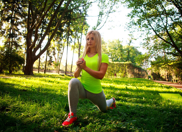 Sportieve slanke vrouw doen fitness oefeningen die zich uitstrekt in park - Foto, afbeelding