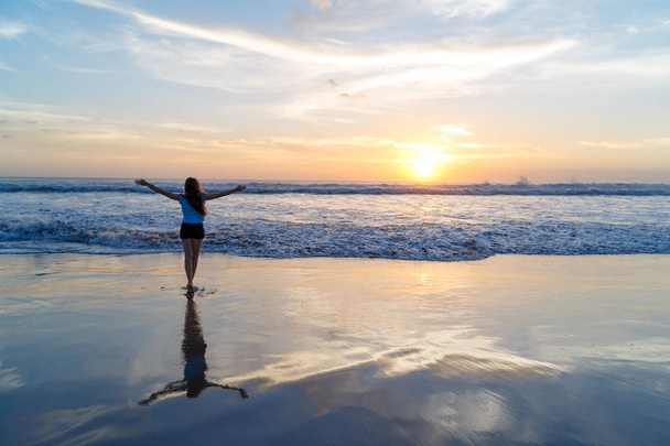 女性が再シルエットの海で夕日の下で腕を開く - 写真・画像