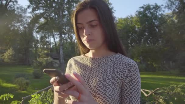 Attractive young woman using her touch screen phone in park 4K  - Metraje, vídeo