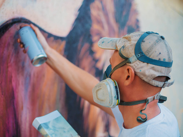 Graffiti Artist Painting On The Street Wall. Man with aerosol spray bottle near the wall. Young talented guy in protective mask drawing colorful lion. - 写真・画像