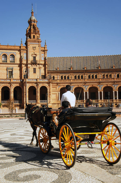 Transporte com rodas amarelas com turistas em frente ao palácio na Praça Espanha (Plaza de Espana) em Sevilha (Sevilha), Espanha
 - Foto, Imagem