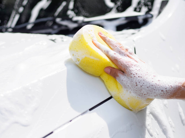 Woman hand with yellow sponge washing car - Foto, afbeelding
