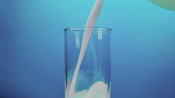 fresh white milk pouring into drinking glass on blue background, shooting with slow motion, diet and healthy nutrition  - Materiał filmowy, wideo
