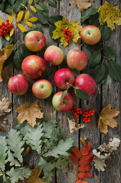 Red apples scattered on the old wooden table with autumn leaves - Foto, Imagem